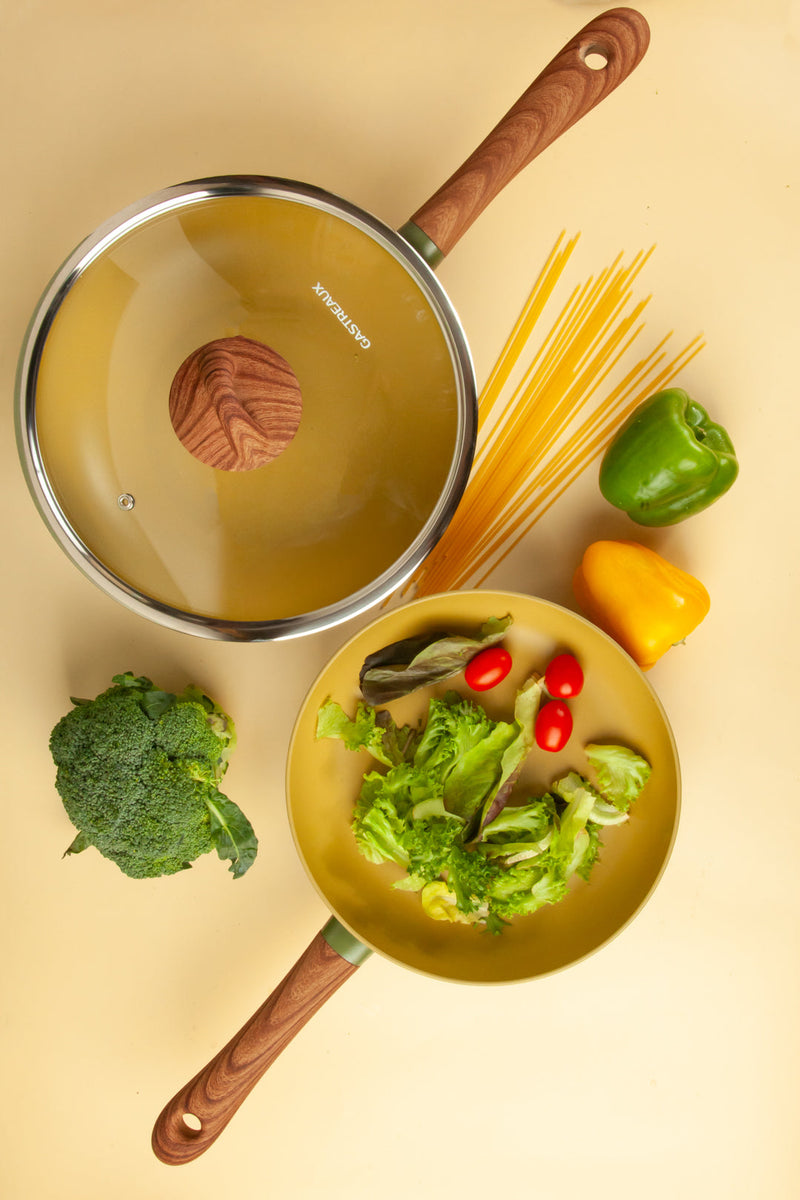 Cookware set with a pan, lid, and vegetables on a beige background
